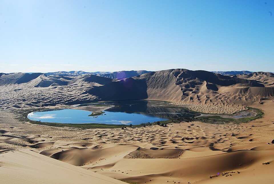 A small lake surrounded by tall dunes near Bilutu in the Badain Jaran Desert