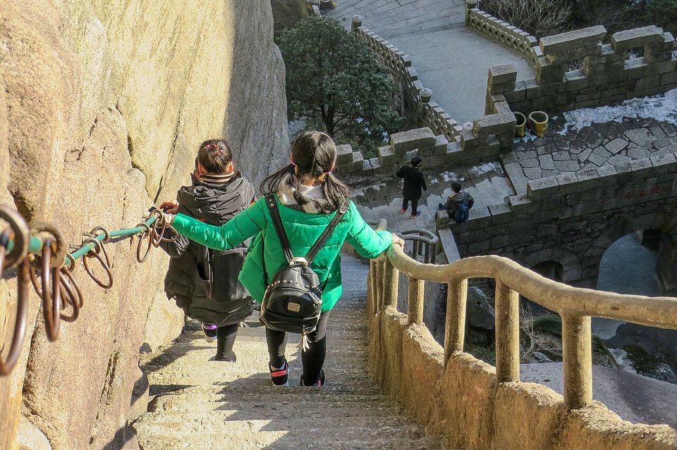 Hikers in winter coats holding a chain railing on a steep granite stairway