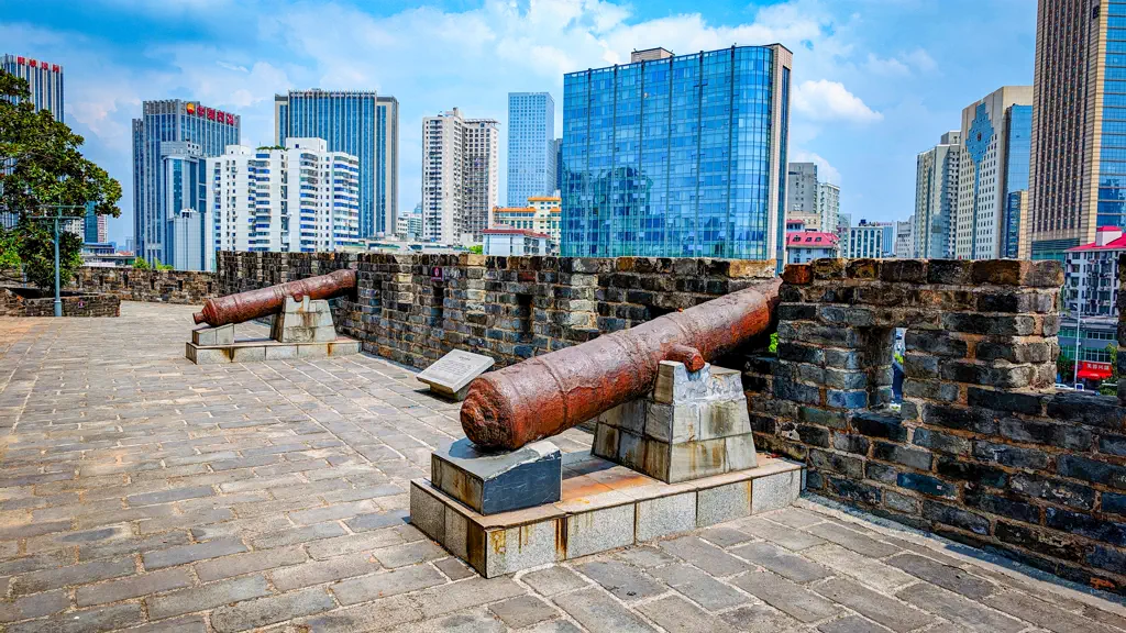 Two antique cannons on the crenellated wall, with modern towers behind