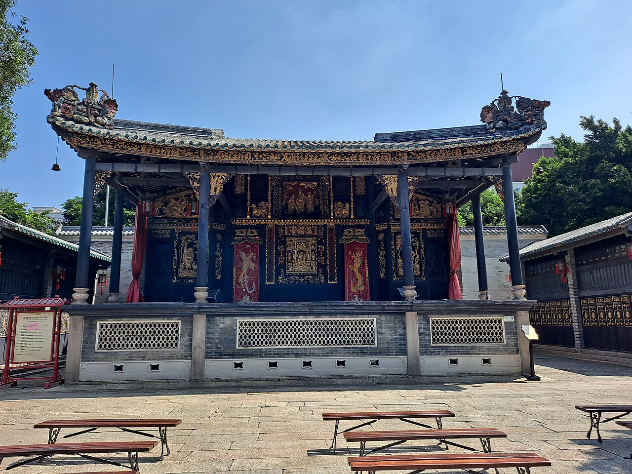 an ornate open-fronted opera stage with gilded carving and dark columns above a stone courtyard