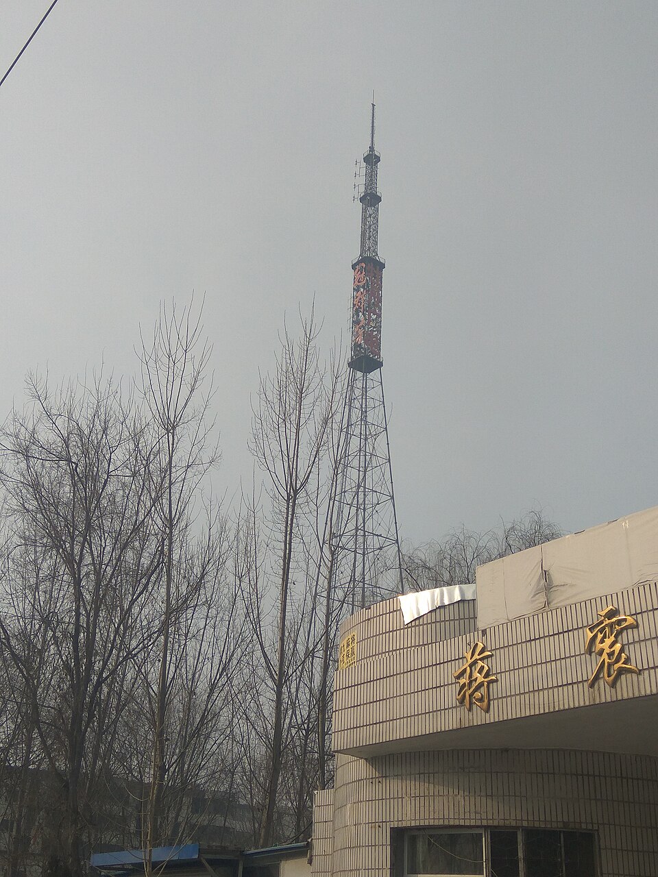 Tall red and white signal tower above low buildings in Mudan District, Heze