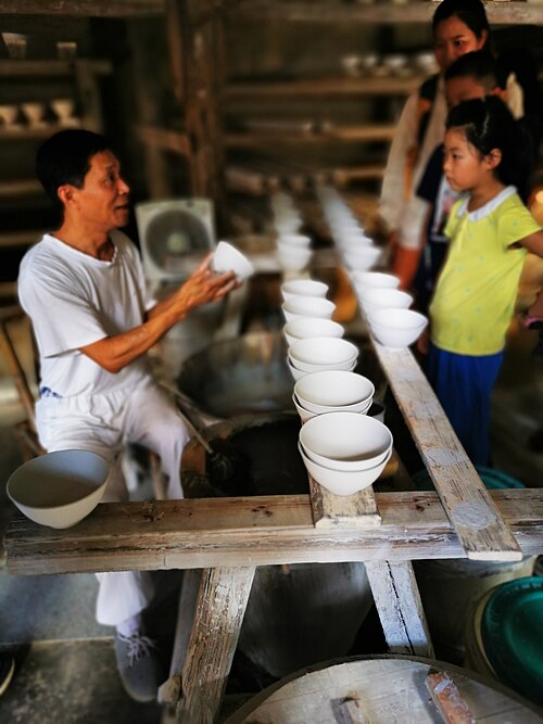 Craftsman holding an unfinished porcelain piece at the Ancient Kiln workshop line