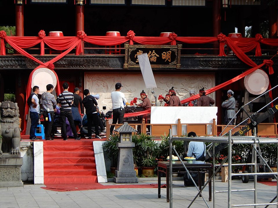 Film crew with cameras and actors in costume on a red decorated set at Hengdian