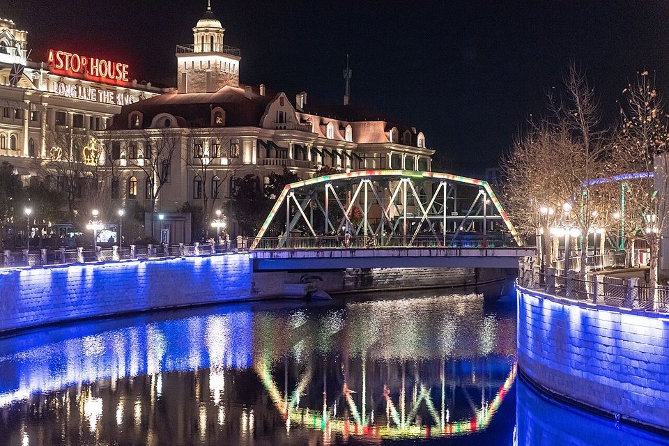 A replica tram crossing a lit steel truss bridge at night at the Legend of Bund set
