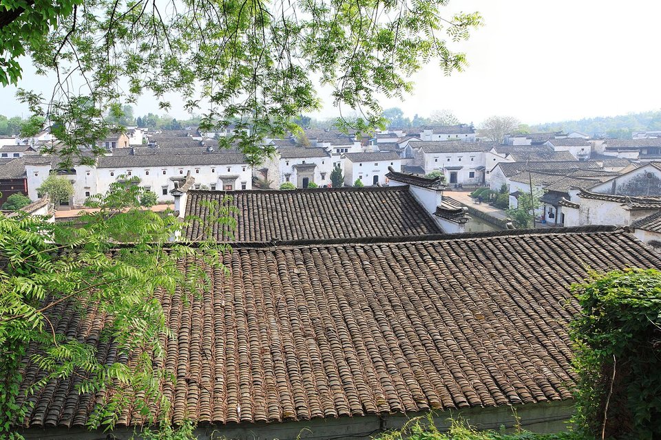 Grey tiled rooftops of Zhuge Village seen over a wall among trees