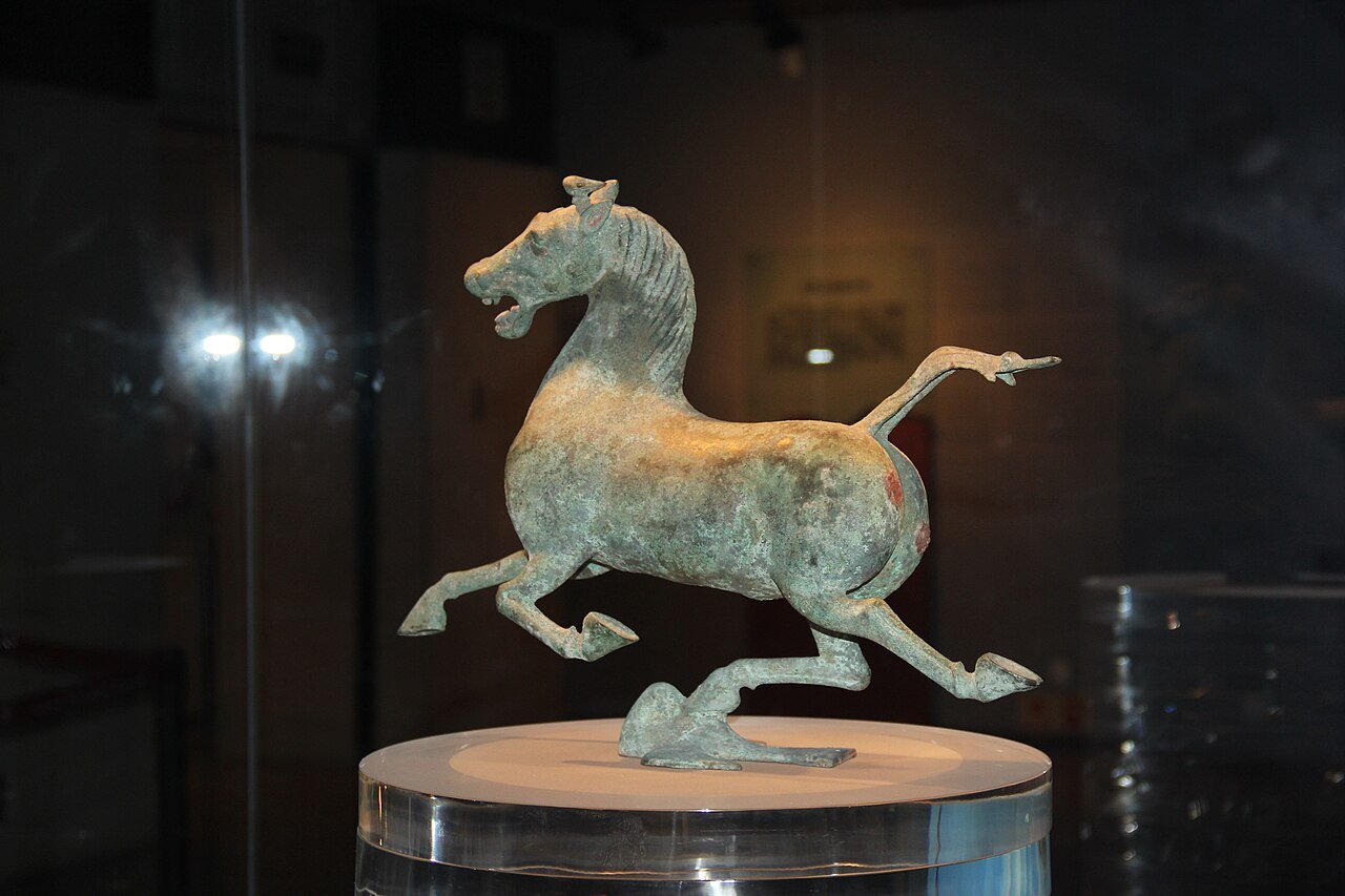 green-patinated bronze horse galloping with one hoof resting on a small bird, displayed on a round plinth