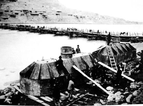 black and white photo of workers on a stone bridge pier in the river with the old pontoon bridge behind