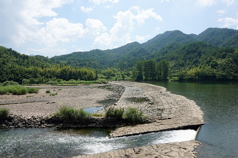 Wide calm river with a pebble bar and forested hills near Tongji Weir