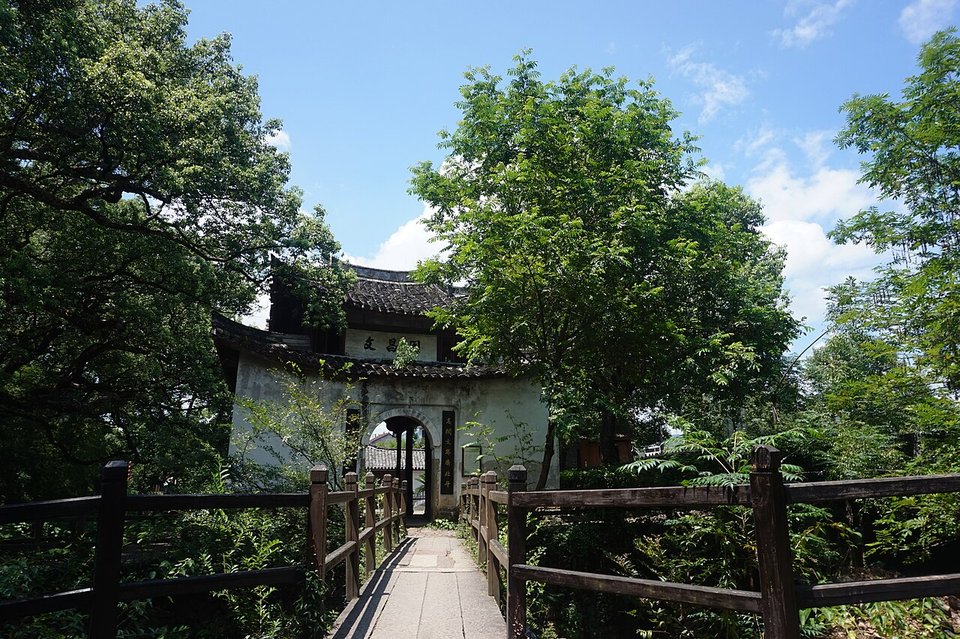 White walled Wenchang Pavilion behind trees at the end of a wooden footbridge in Yantou village