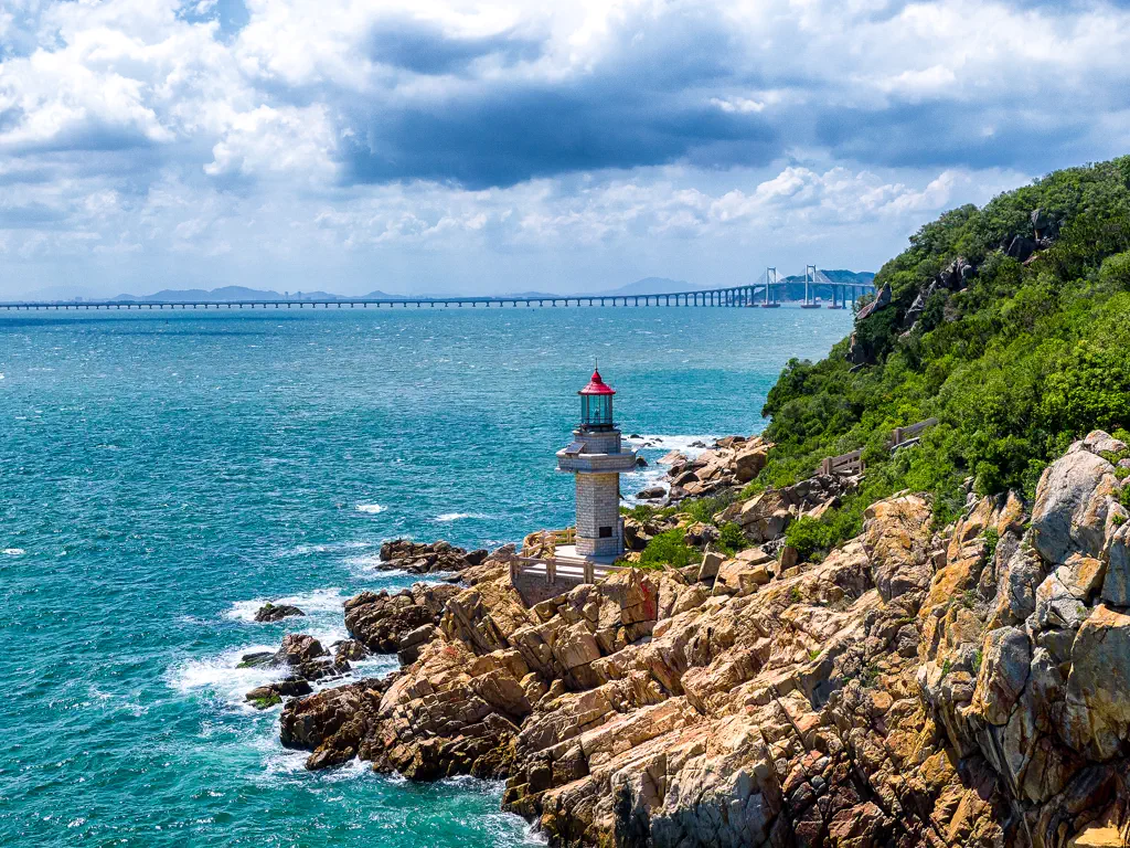 A lighthouse on the rocks with the Nan'ao Bridge in the distance
