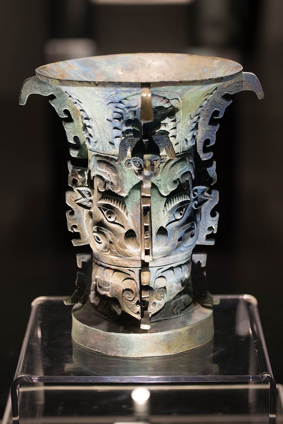 Early bronze zun wine vessel with tall flanges and animal-mask decoration in a display case