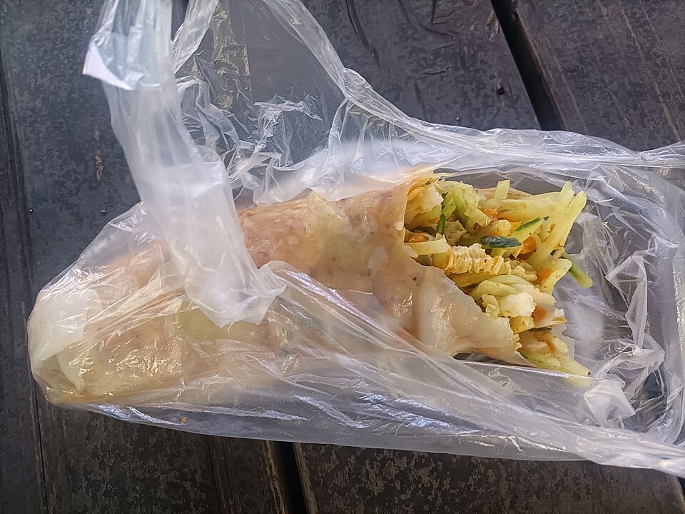 Thin flatbread wrapped around shredded egg and vegetables in a plastic bag, a street breakfast in Xiao County