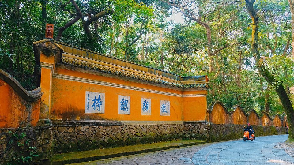 Long ochre wall of Guoqing Temple with black characters beside a stream and trees