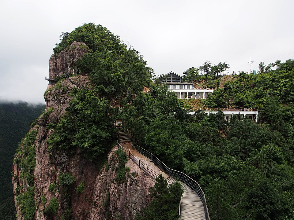 Cliff-hugging walkway climbing a forested rock pillar at Shenxianju