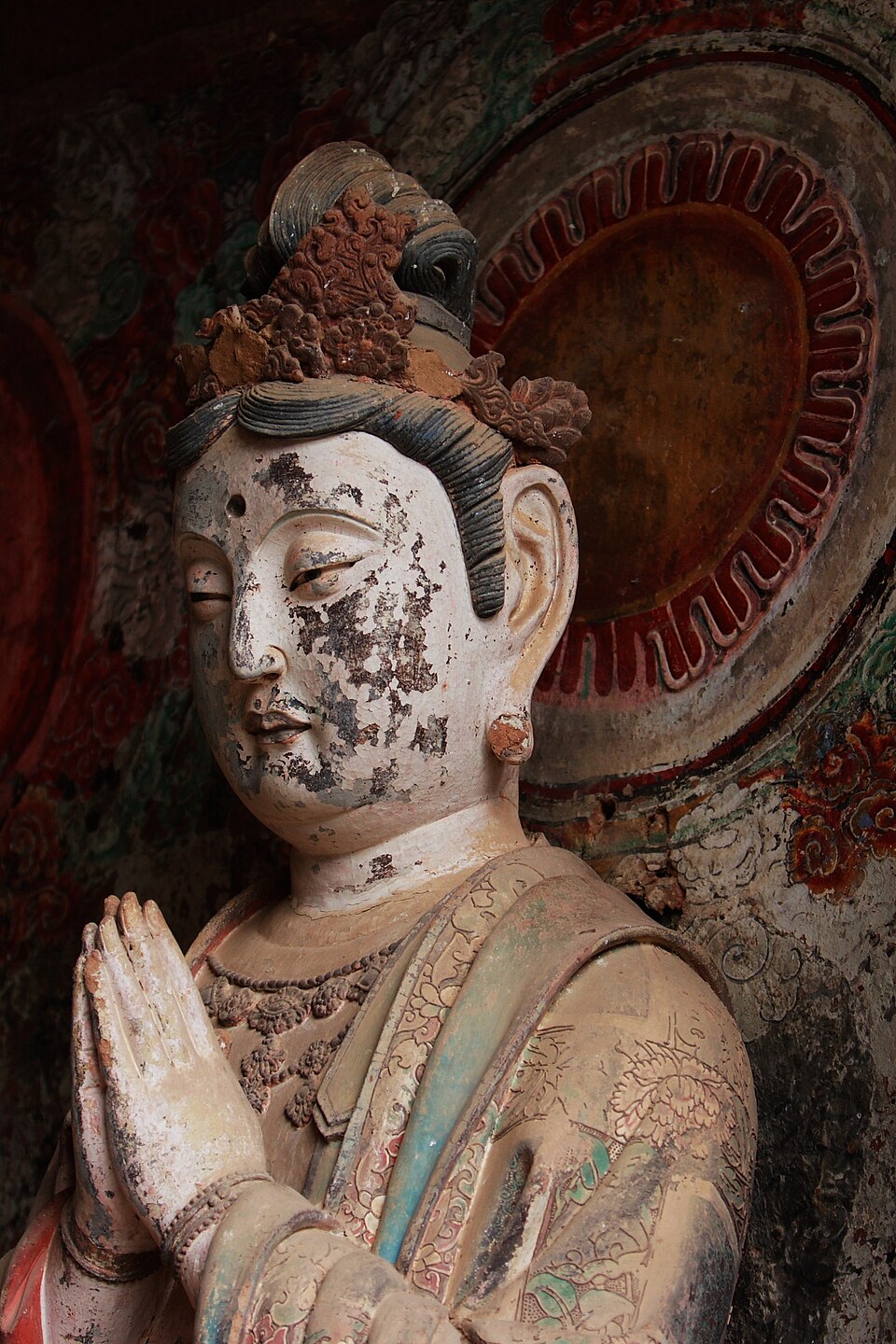Painted clay bodhisattva with palms pressed together and a calm smile at Maijishan
