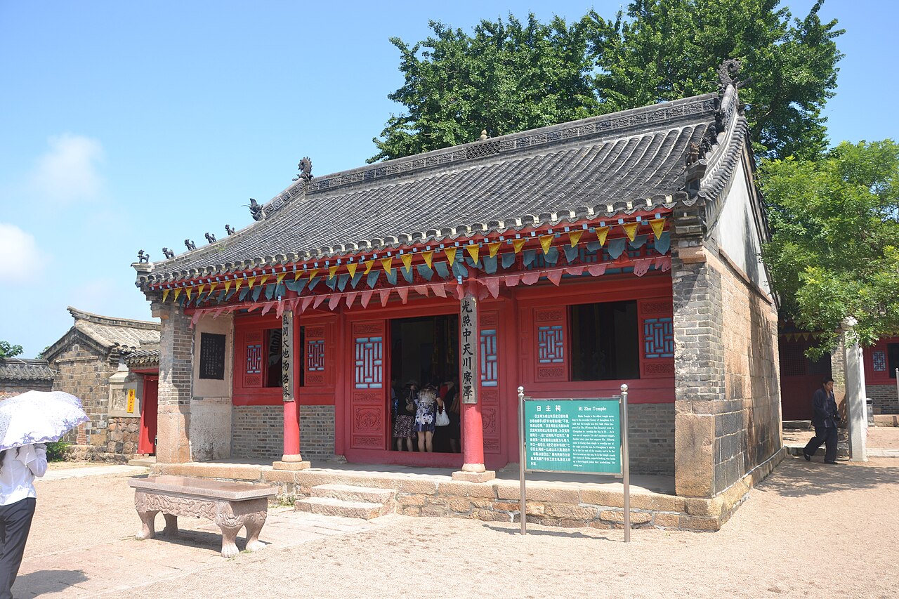 a small Chinese temple hall with red pillars and grey roof tiles beside trees