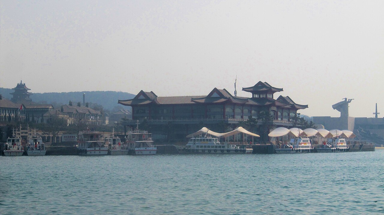 Ferry terminal with traditional roofs and moored boats on Liugong Island, seen across the water