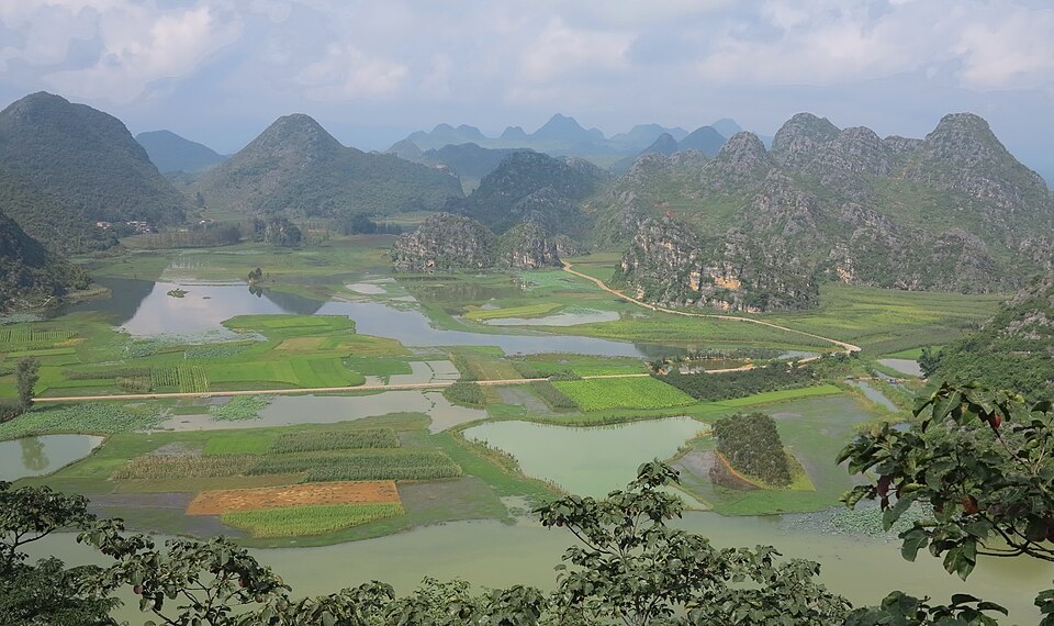 Wide view of karst cones, ponds and patchwork fields under cloud at Puzhehei