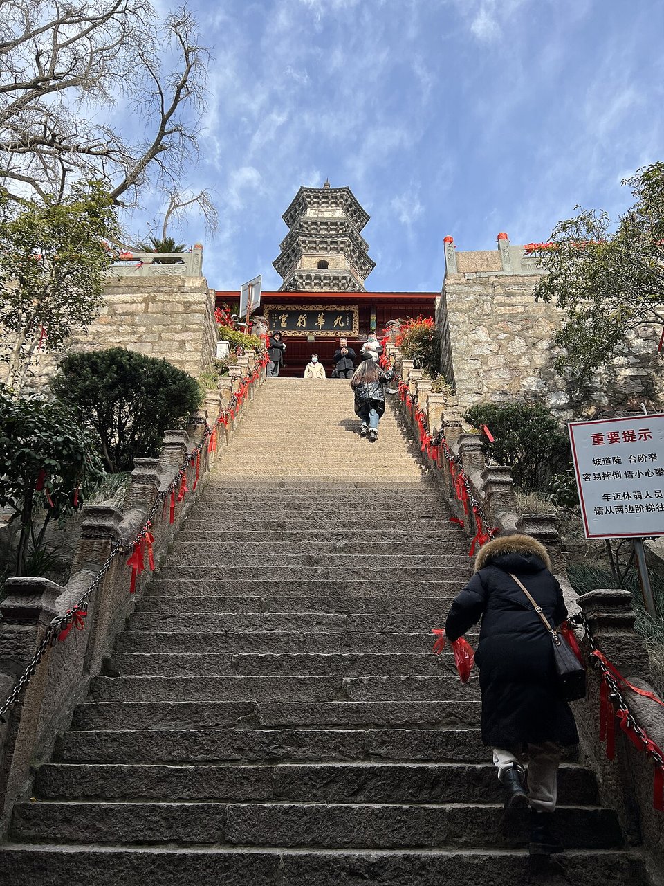 Steep stone staircase lined with red walls climbing to a temple gate and pagoda