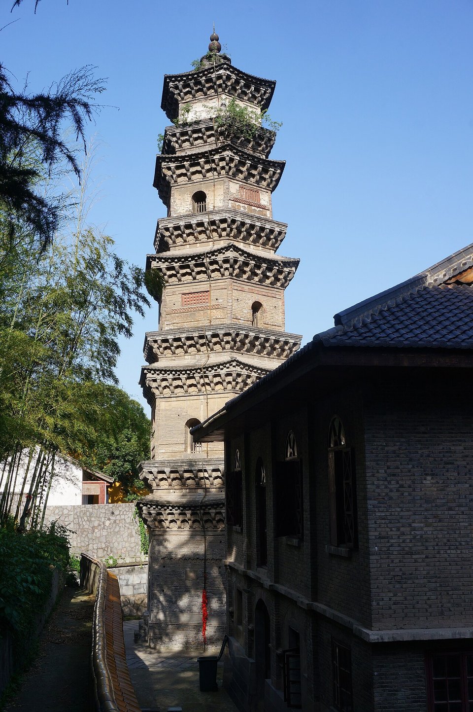 Tall hexagonal brick Zheta Pagoda with tiered eaves beside the roof of a temple hall