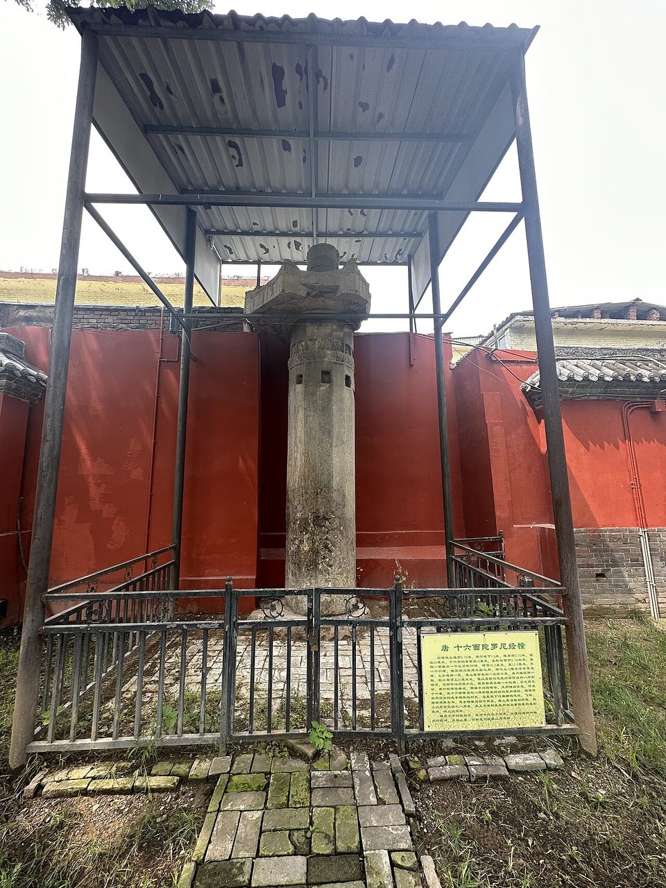 Tall weathered sixteen-sided Tang dharani pillar under a protective canopy at Kaiyuan Temple