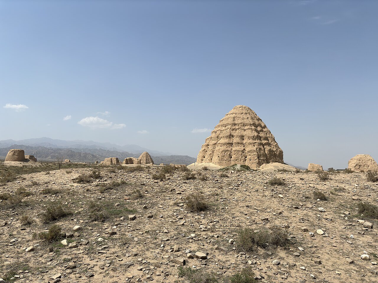a conical earthen mound in desert scrub with smaller ruins and the Helan Mountains in the distance