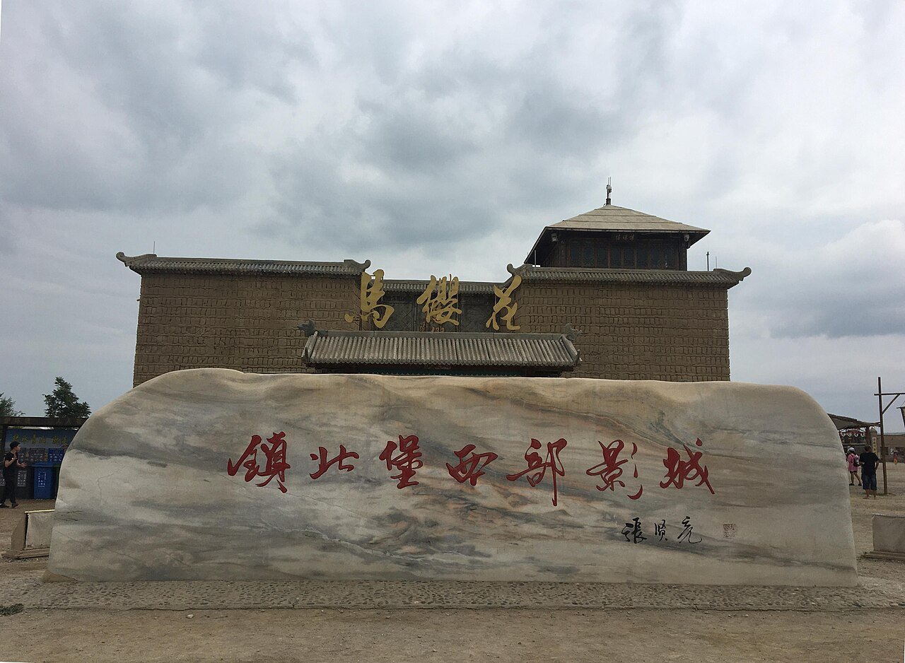 a carved stone at the entrance reading Zhenbeipu Western Film Studio in red characters with an earthen fort tower behind