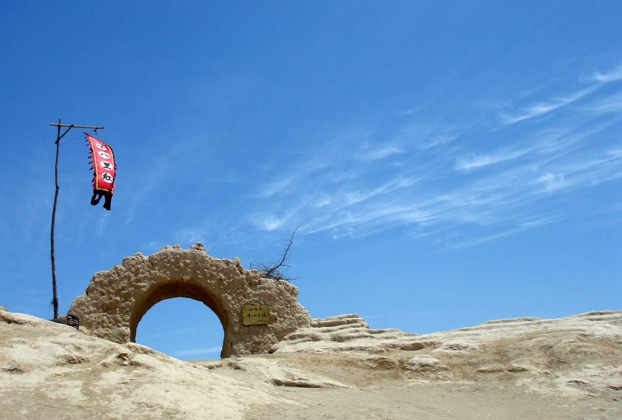 a round arched gateway in a crumbling earth wall against a deep blue sky with a red flag on a pole